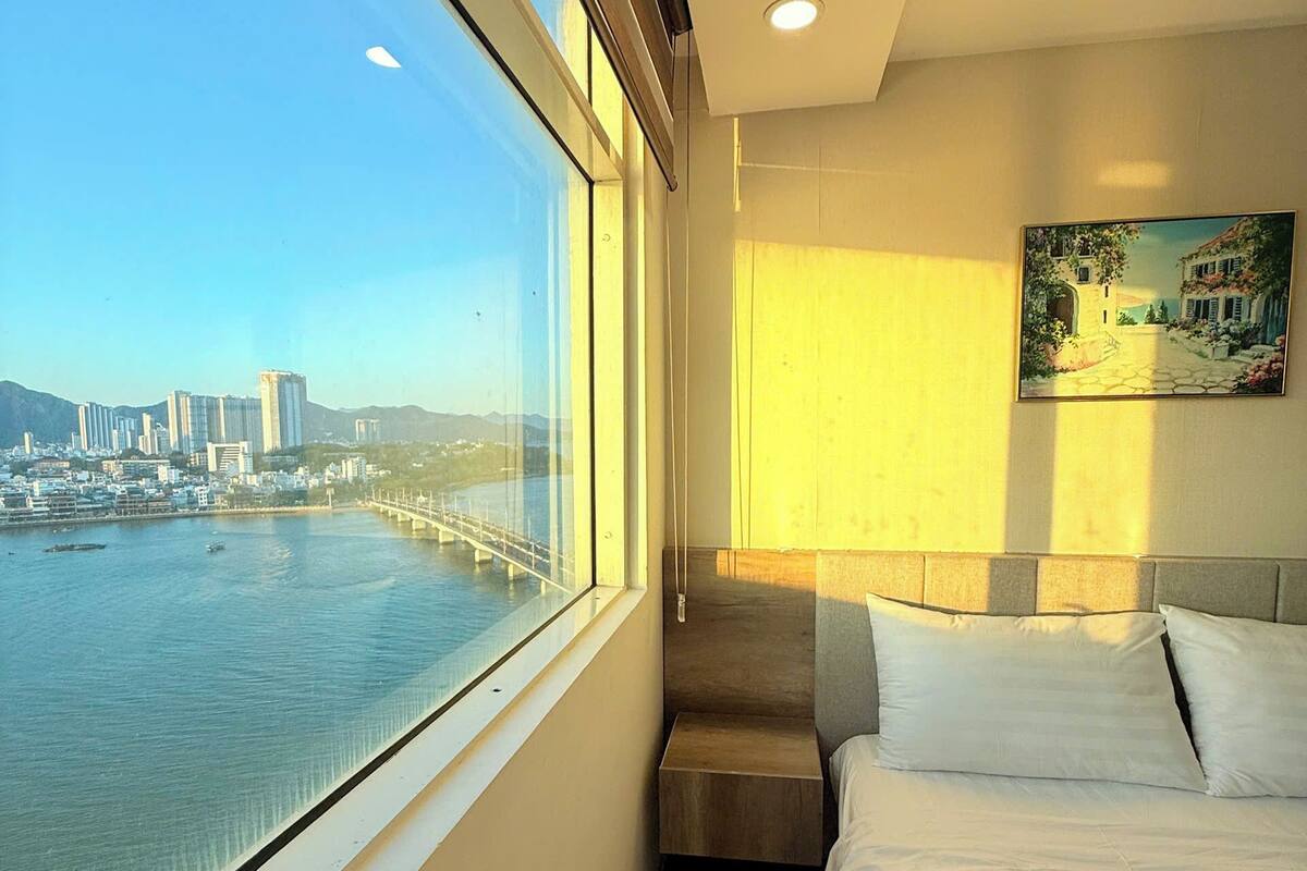 Quarto de hotel com cama, janela com vista para a cidade, quadro na parede e cabeceira.