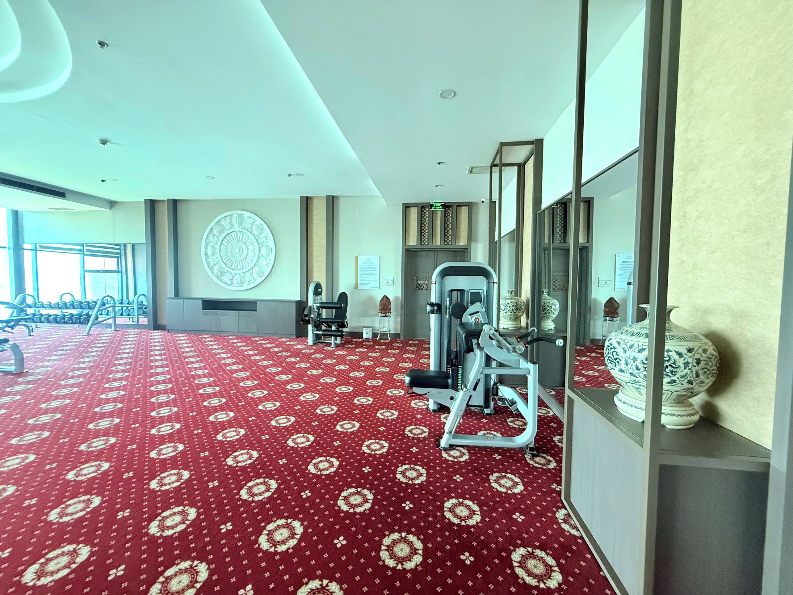 A gym with exercise equipment, a patterned carpet, and decorative vases.