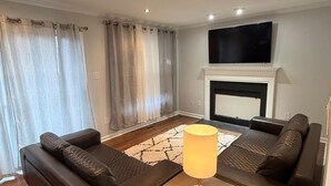 Una sala de estar con un juego de sofá, una mesa de centro, un televisor sobre la chimenea y piso de madera.