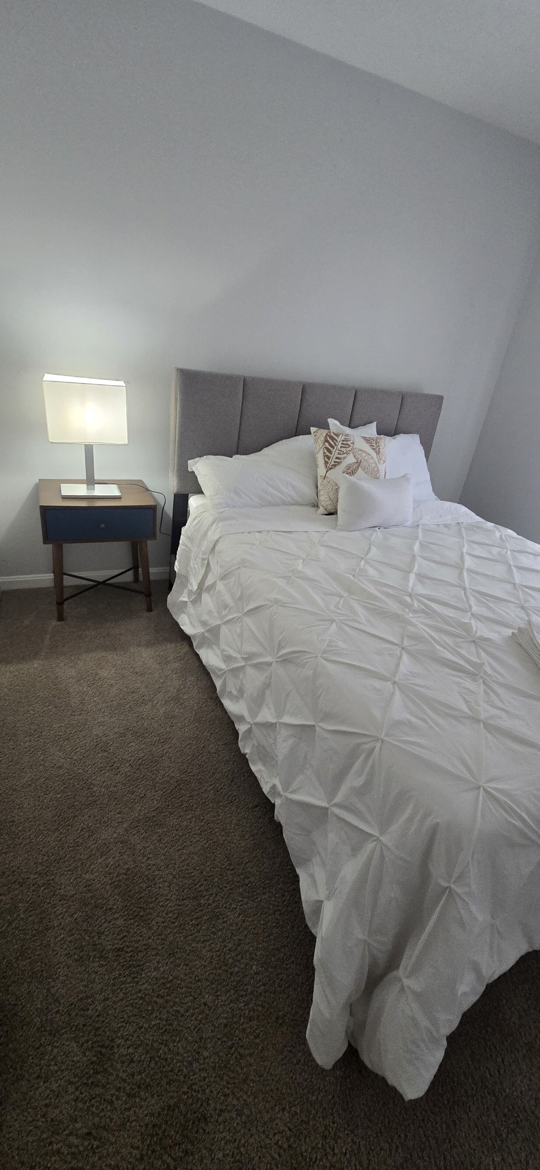 A bedroom with a bed, a nightstand, a lamp, and a carpeted floor.