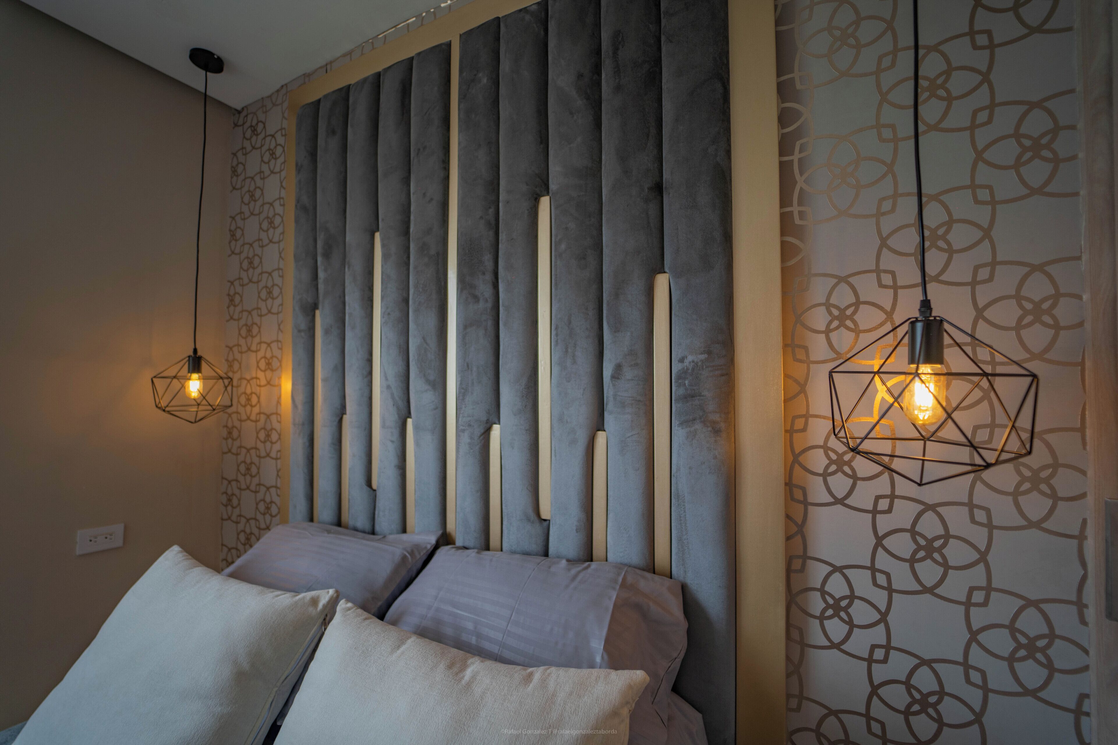 A bedroom with a bed, a headboard with vertical slats, and two pendant lights.