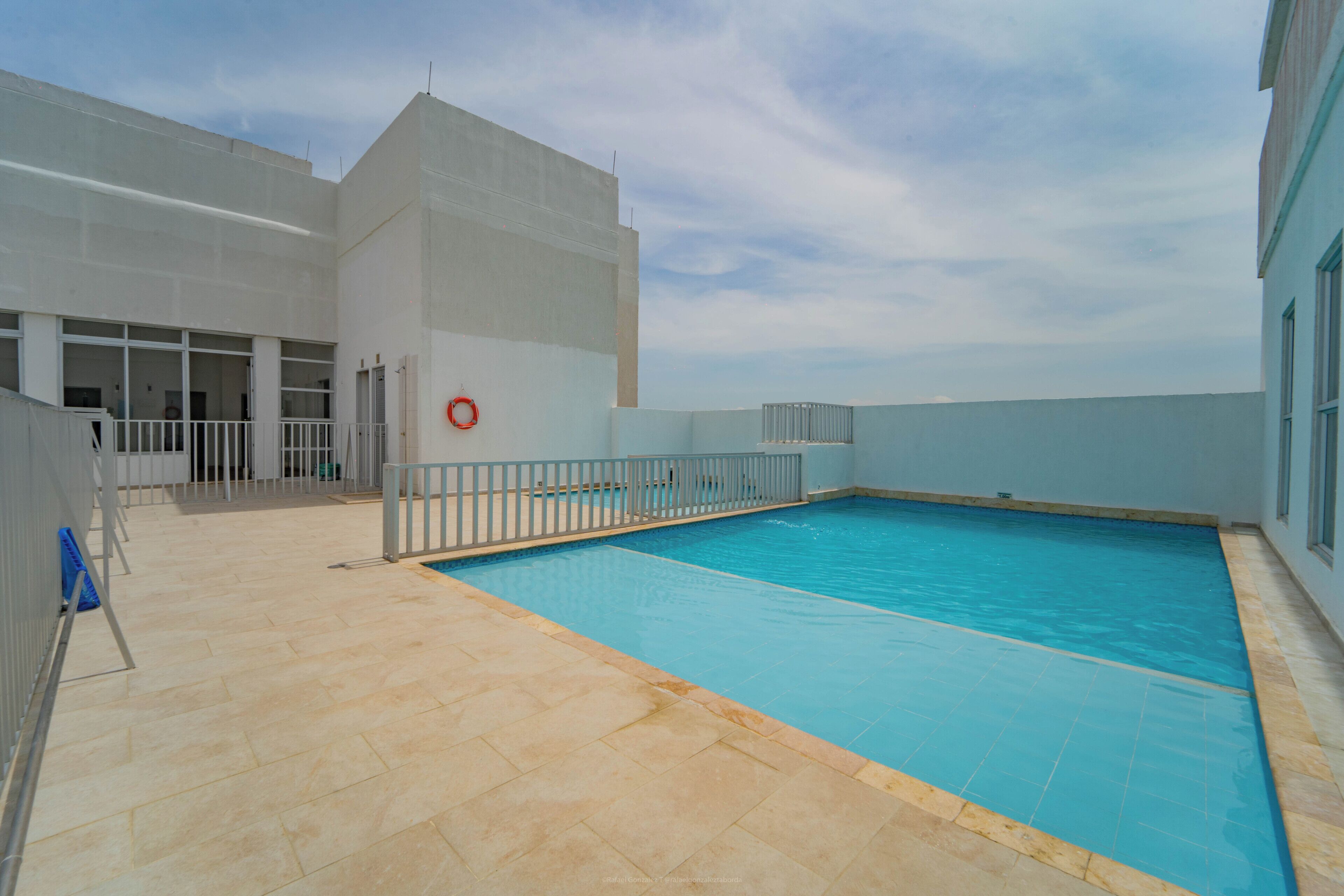 An indoor swimming pool with a tiled floor, a lifebuoy on the wall, and a white railing around the pool.