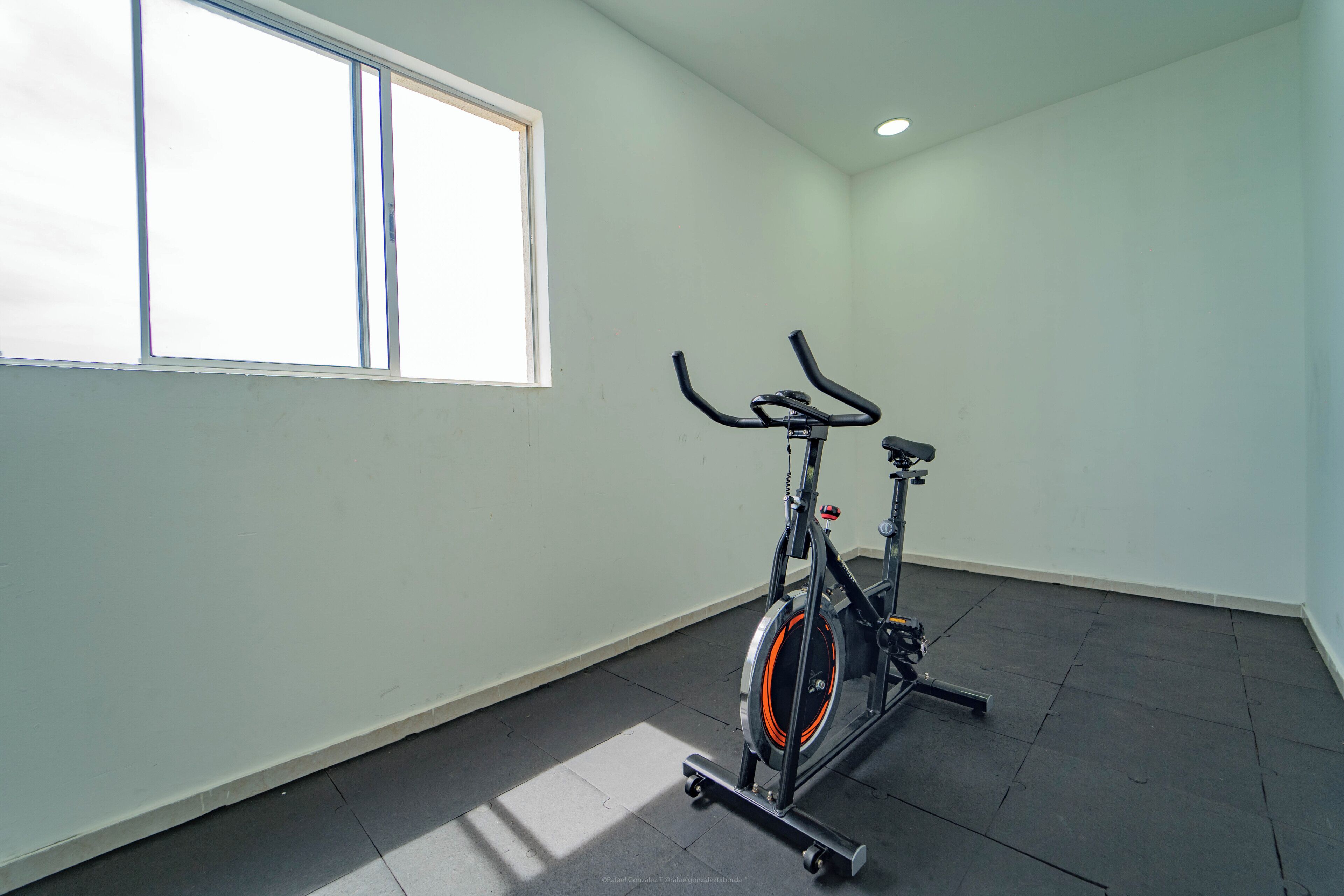 A room with a standing exercise bike, a large window, and a tiled floor.