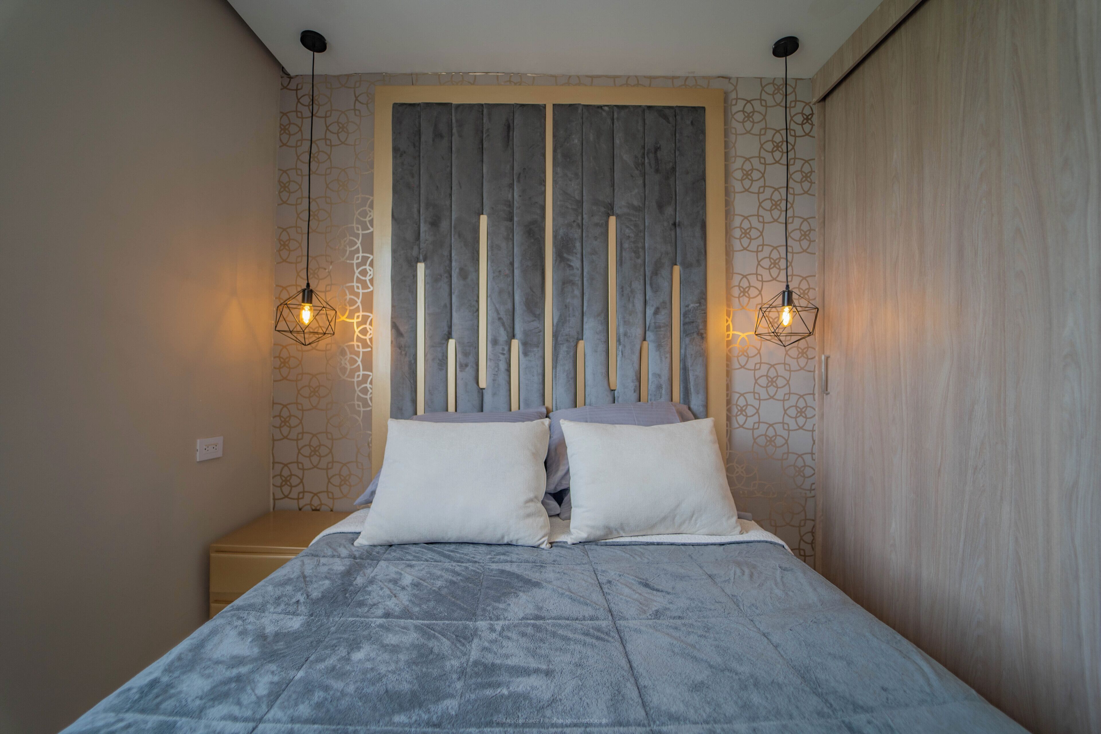 Ein Schlafzimmer mit einem Bett, zwei Nachttischlampen, einem Kopfteil und einer Wand mit Muster.