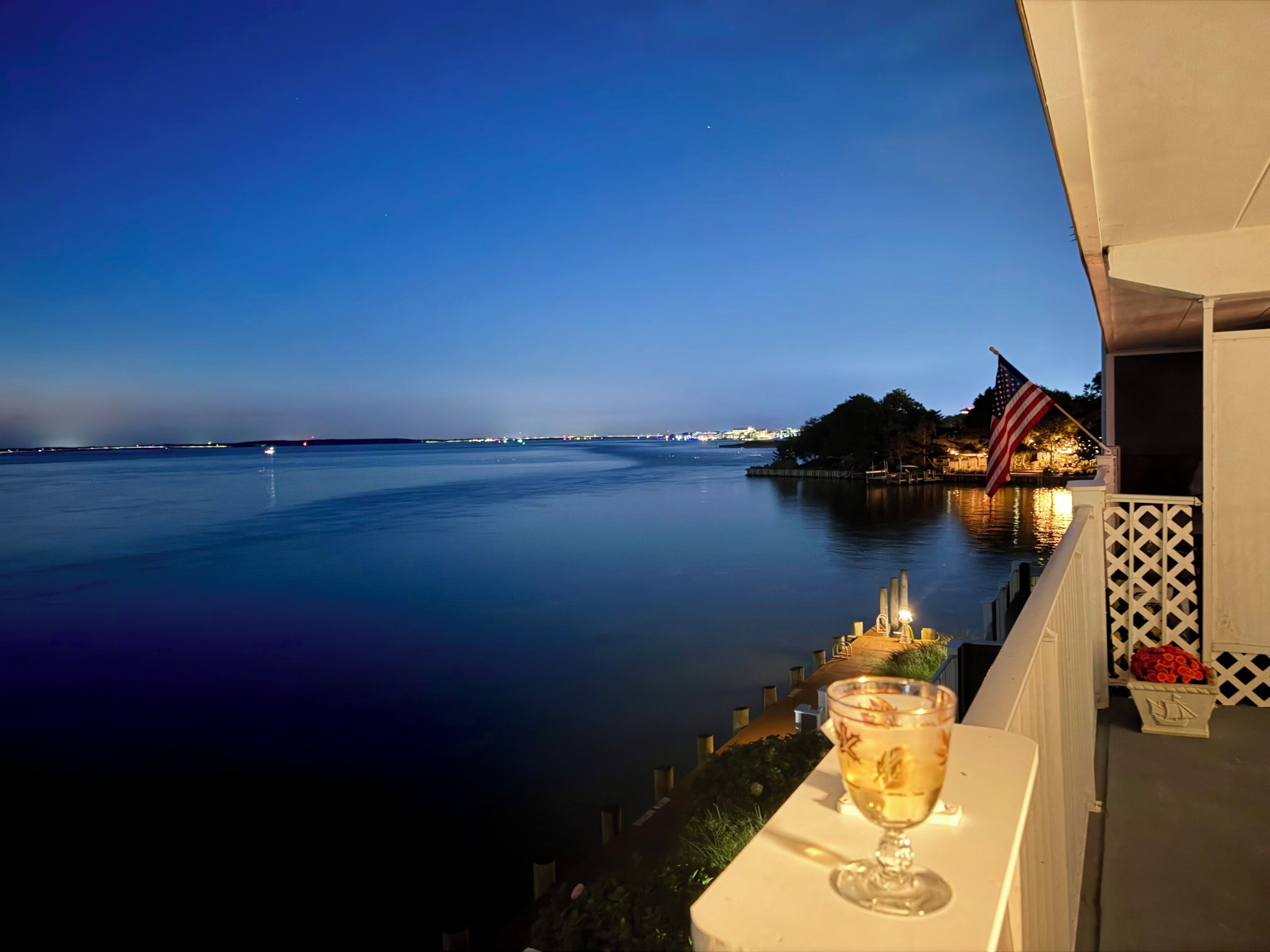 Un balcone con vista su una distesa d'acqua tranquilla, una bandiera americana e un bicchiere di bevanda.