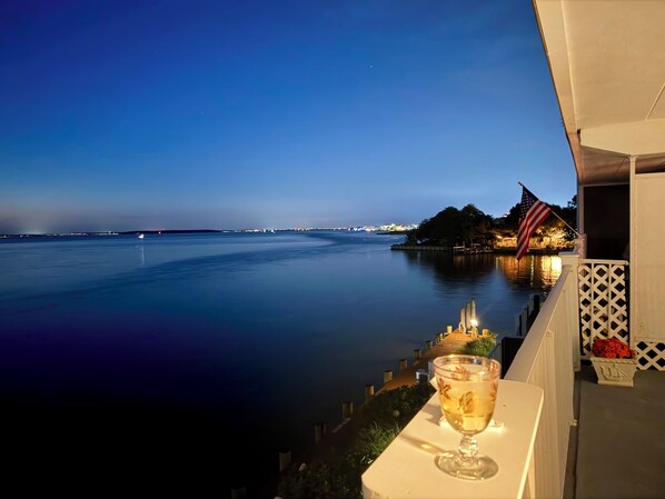 A balcony with a view of a calm body of water, an American flag, and a glass of a beverage. - Waterfront Harbour Island Downtown Stunning Bay View Walk to Beach & Boardwalk (Ocean City)