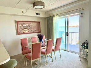 A dining area with a glass table, red chairs, a framed artwork, and a view of the sea through a sliding door. - Ocean City MD Harbour Island Bay View Condo (Ocean City)