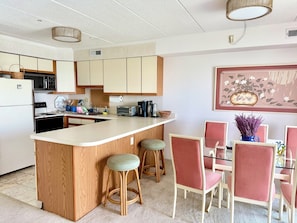 Una cocina con una isla central, armarios de madera, un refrigerador y un comedor con mesa y sillas.