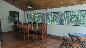 Un comedor con una mesa y sillas de madera, un ventilador de techo y una ventana con vistas a árboles.