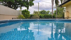 En swimmingpool med klart, blåt vand, omgivet af et hegn og træer.