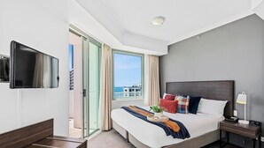 A hotel room with a bed, a TV, a bedside table with a lamp, and a window with curtains. - Skyline Hideaway Studio (Gold Coast)