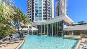 A swimming pool with lounge chairs, surrounded by tall buildings and palm trees. - Skyline Hideaway Studio (Gold Coast)