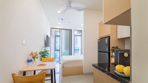 A compact kitchen with a refrigerator, a dining table with chairs, and a window with a view of buildings. - LINH KHANG 1 Hotel & Apartment Da Nang (Da Nang)