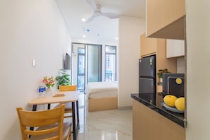 A compact kitchen with a refrigerator, a dining table with chairs, and a window with a view of buildings. - LINH KHANG 1 Hotel & Apartment Da Nang (Da Nang)