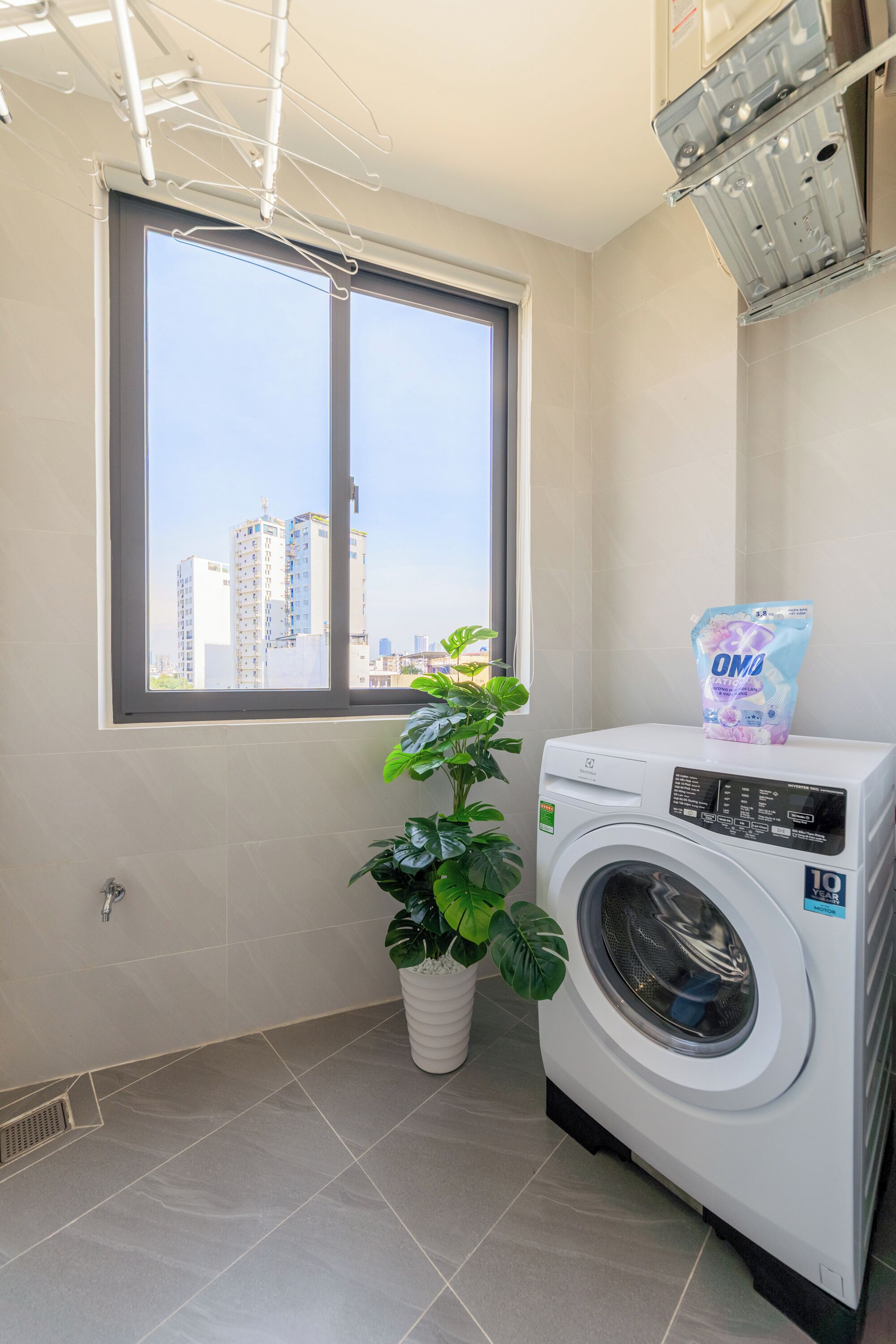 A laundry room with a washing machine, a window with a view of buildings, and a potted plant.