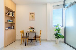 A small dining area with a table, chairs, a potted plant, and a shelf with books and a kettle. - LINH KHANG 1 Hotel & Apartment Da Nang (Da Nang)