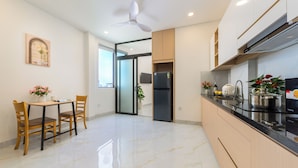 A modern kitchen with a refrigerator, stove, and dining area with chairs and a table. - LINH KHANG 1 Hotel & Apartment Da Nang (Da Nang)