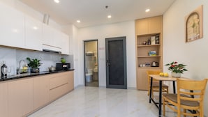 A modern kitchen with white cabinets, a marble countertop, and a dining area with a table and chairs. - LINH KHANG 1 Hotel & Apartment Da Nang (Da Nang)