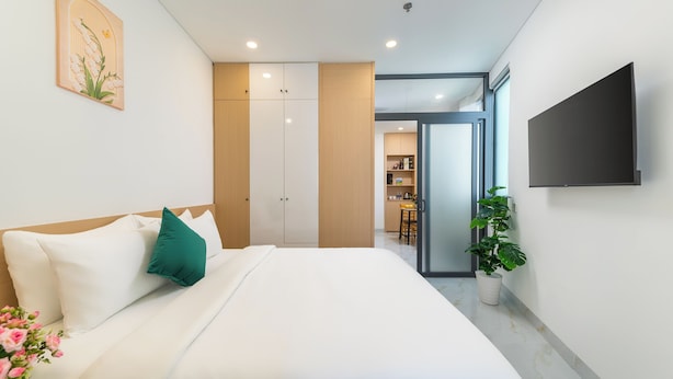 A modern hotel room with a bed, a flat-screen TV, a potted plant, and a view into the kitchen area. - LINH KHANG 1 Hotel & Apartment Da Nang (Da Nang)