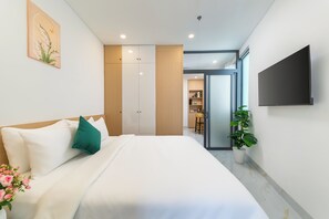 A modern hotel room with a bed, a flat-screen TV, a potted plant, and a view into the kitchen area. - LINH KHANG 1 Hotel & Apartment Da Nang (Da Nang)