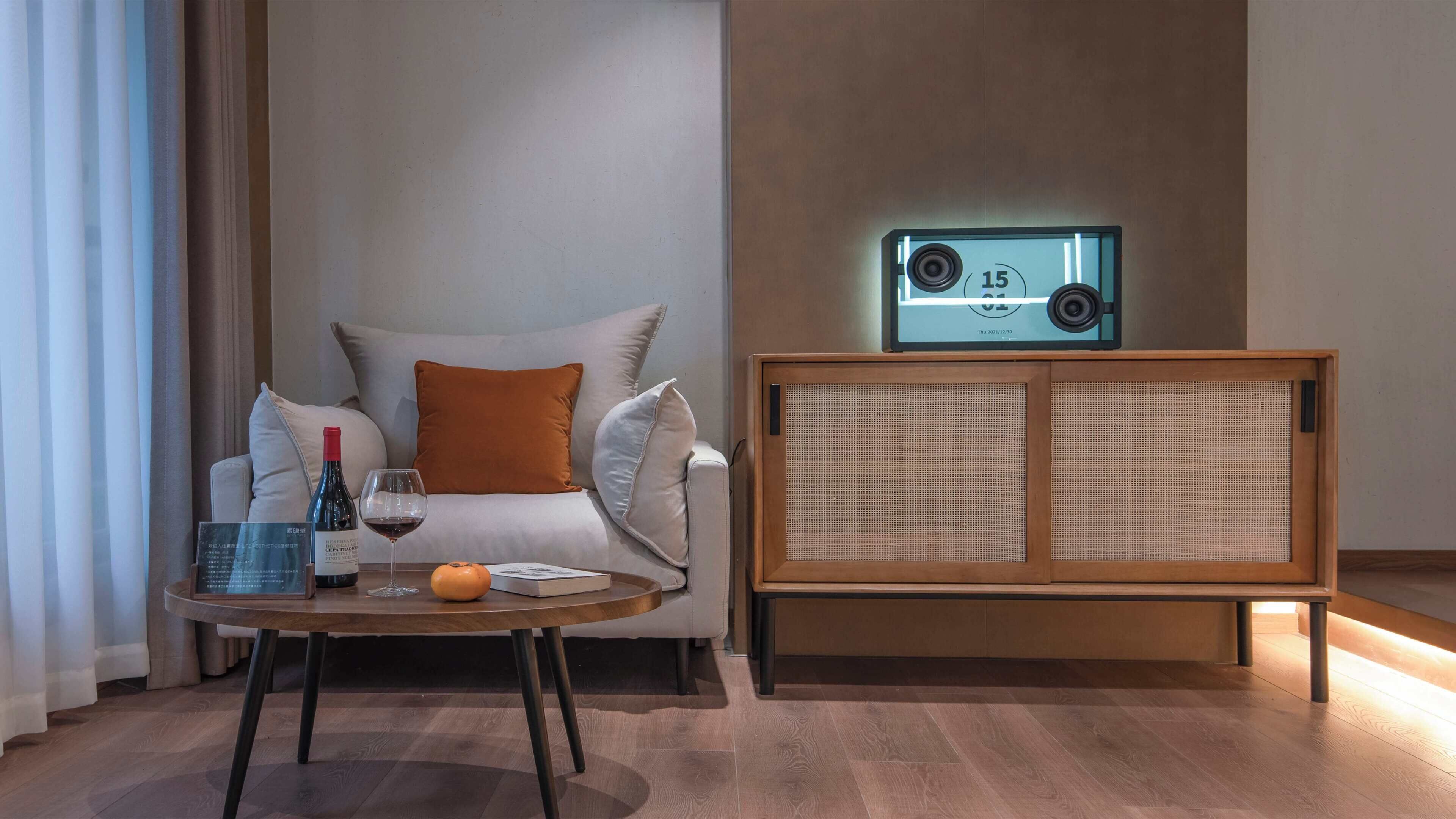 Una sala de estar moderna con un sofá, una mesa baja con una botella y un vaso, y un mueble de madera con un altavoz.