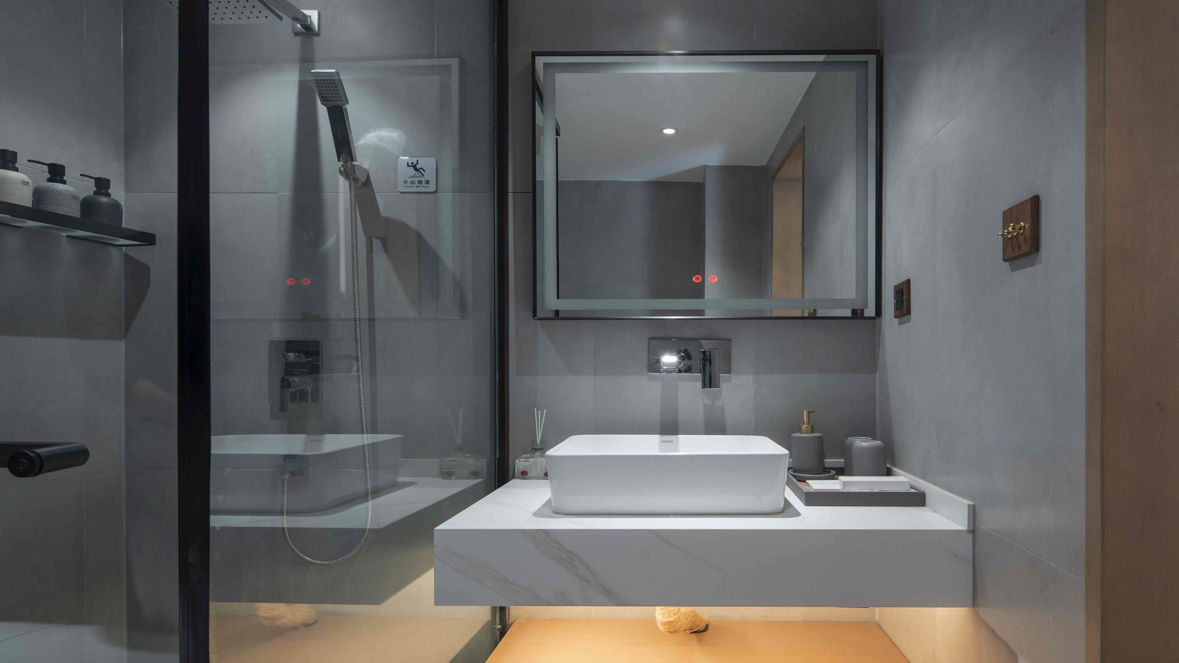 A modern bathroom with a glass-enclosed shower, a large mirror, and a white sink.