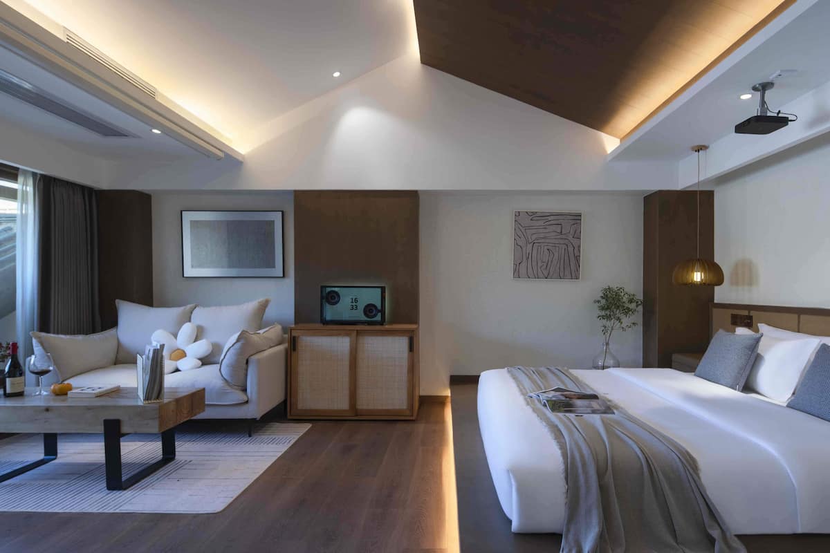 A modern hotel room with a bed, a sofa, a small table with a wine bottle, and a radio.