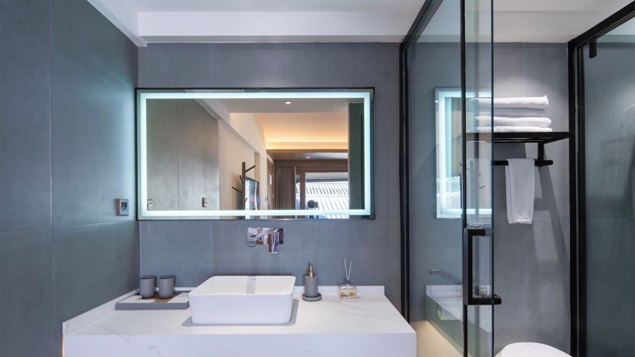 A modern bathroom with a large mirror, a white sink, and a glass shower enclosure.