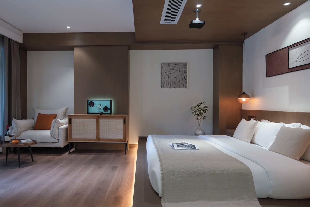 A hotel room with a bed, a sofa, a small table with a wine bottle, and a decorative item on the wall.