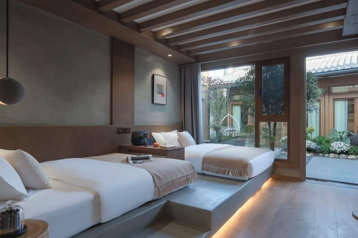 A modern hotel room with two beds, a large window, and a view of the garden.