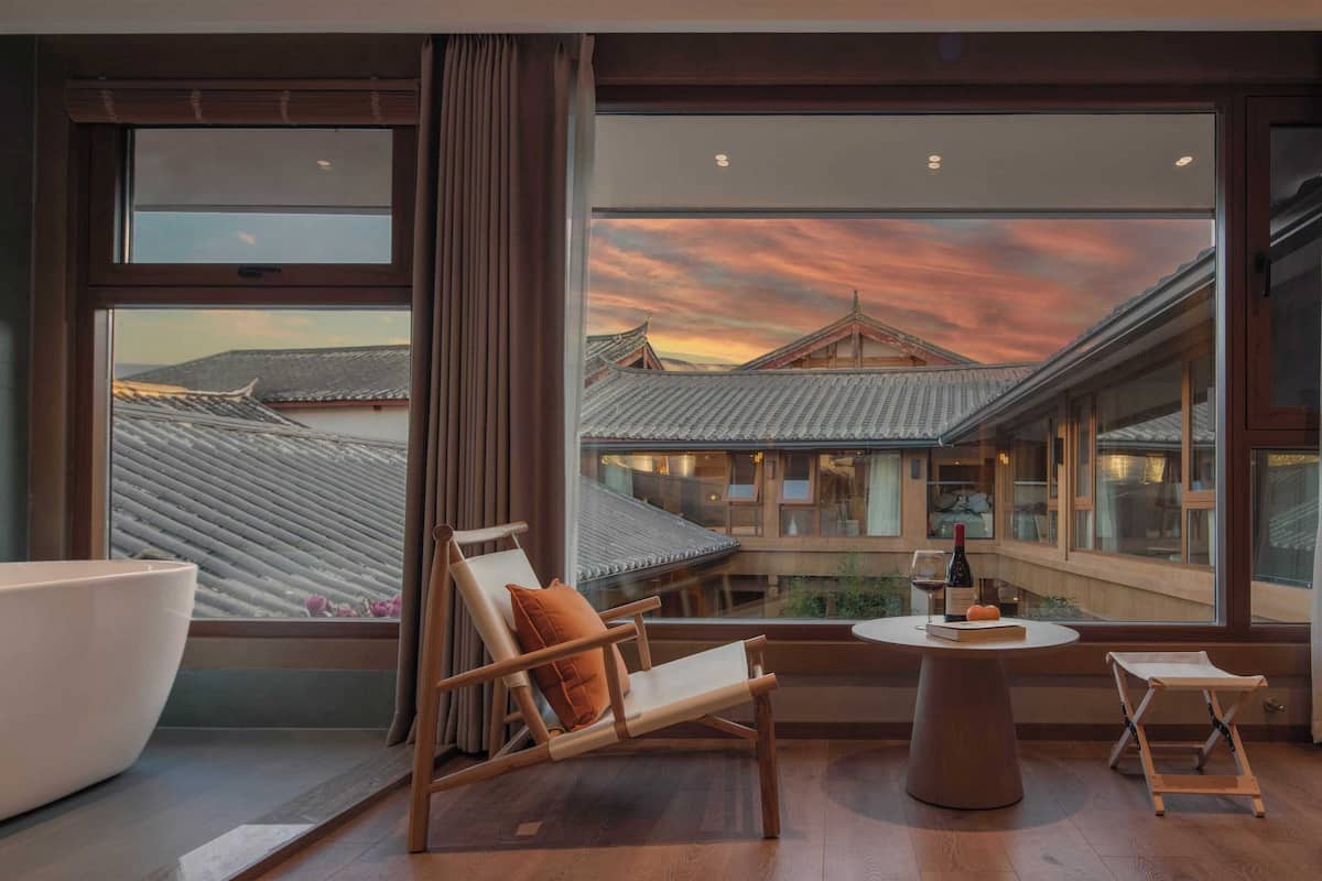 A room with a traditional wooden chair, a round table, and a view of a traditional building through large windows.