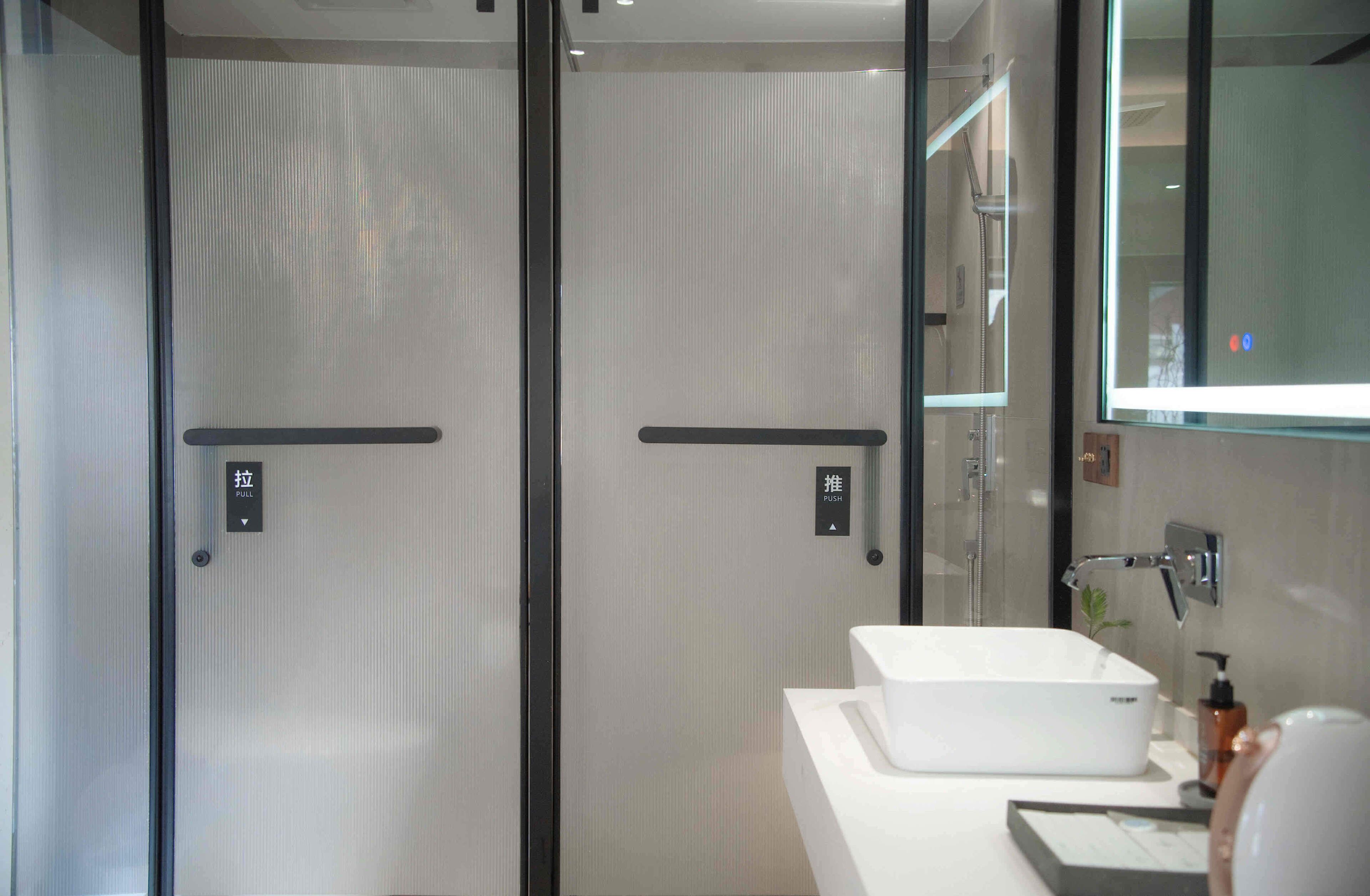 A modern bathroom with two glass doors, a white sink, and a mirror.