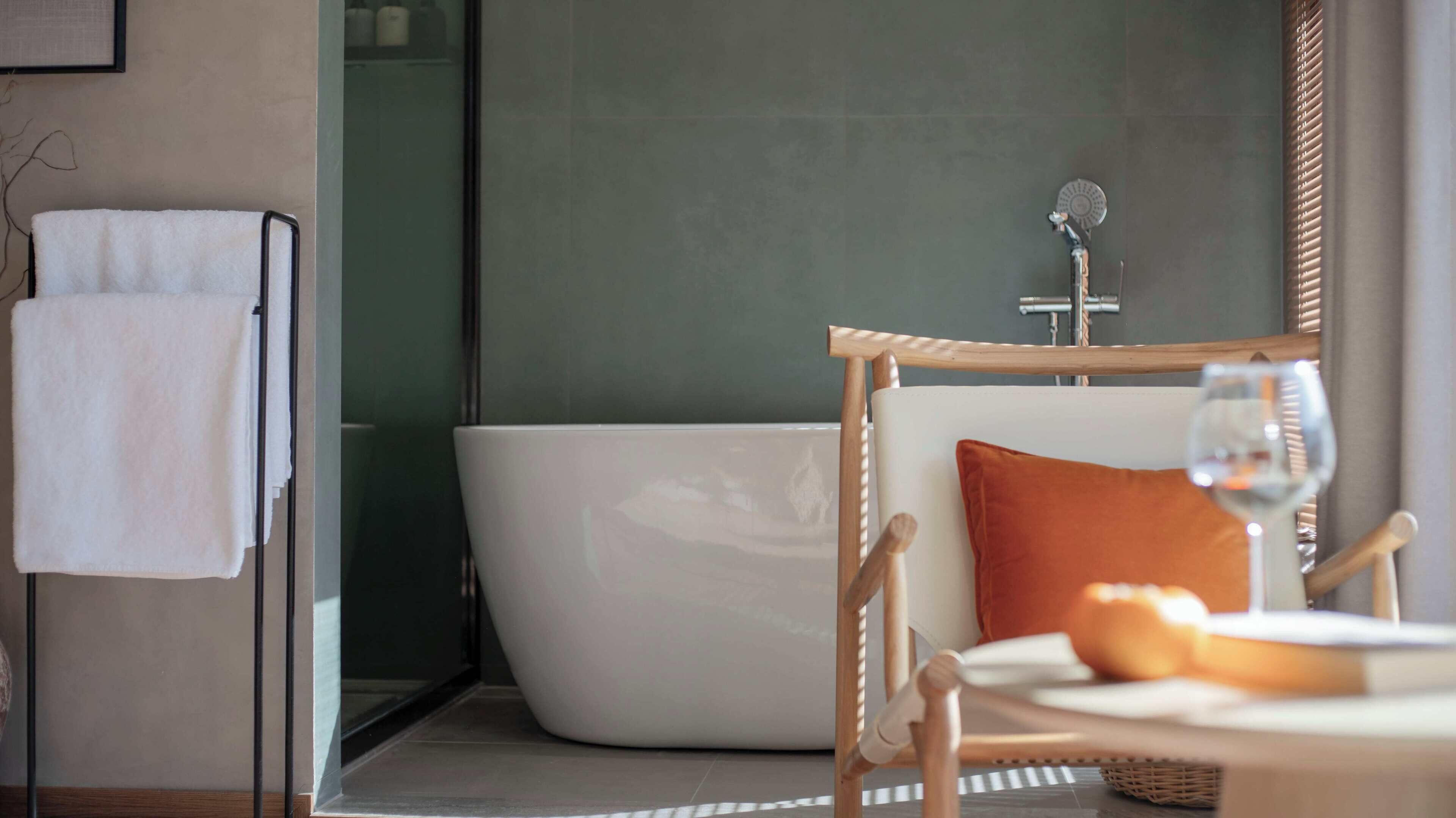 A modern bathroom with a bathtub, a towel rack, and a wicker chair with a glass of wine.