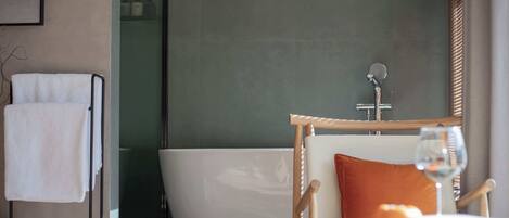 A modern bathroom with a bathtub, a towel rack, and a wicker chair with a glass of wine.