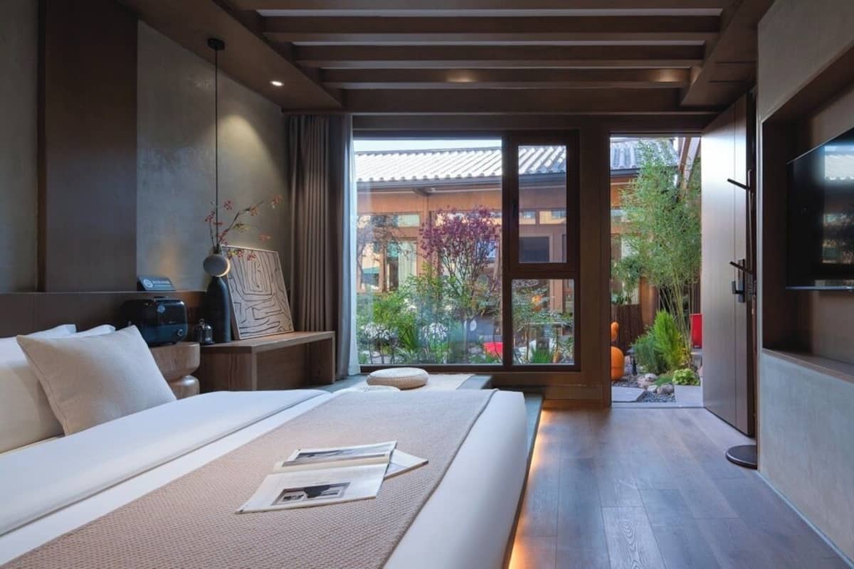 A modern hotel room with a large bed, a TV, and a view of a garden through a sliding door.