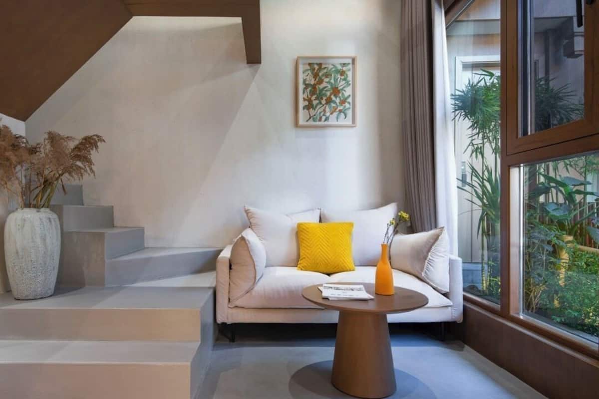 A modern interior with a sofa, a vase, and a window with a view of greenery.