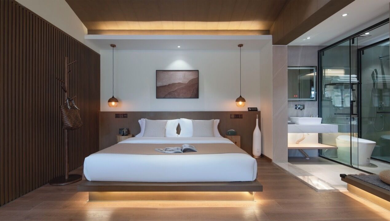 A modern hotel room with a large bed, bedside tables, a glass shower enclosure, and a wooden accent wall.