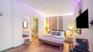 Moderni hotellihuone, jossa on sänky, yöpöydät, televisio ja kahvinkeitin.