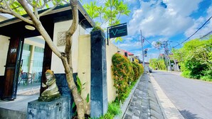 A building with a sign reading 'Ganggu Dormitory,' a statue, a tree, and a paved sidewalk. - V Canggu Dormitory (Tibubeneng)