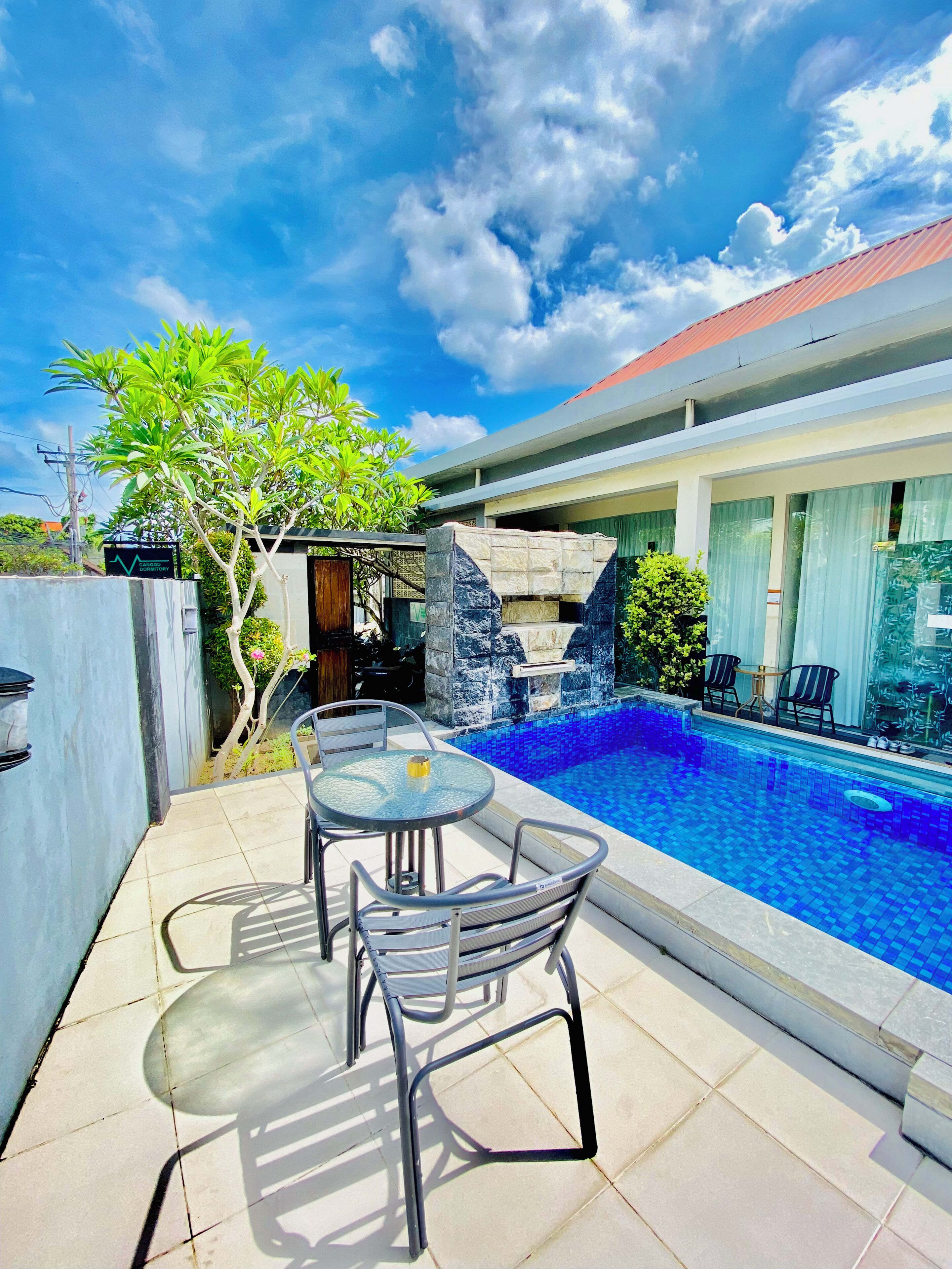 A swimming pool with a tiled deck, a table with chairs, and a stone structure.