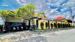 A building with a red roof, a gated entrance, and a row of neatly trimmed bushes along the side. - V Canggu Dormitory (Tibubeneng)
