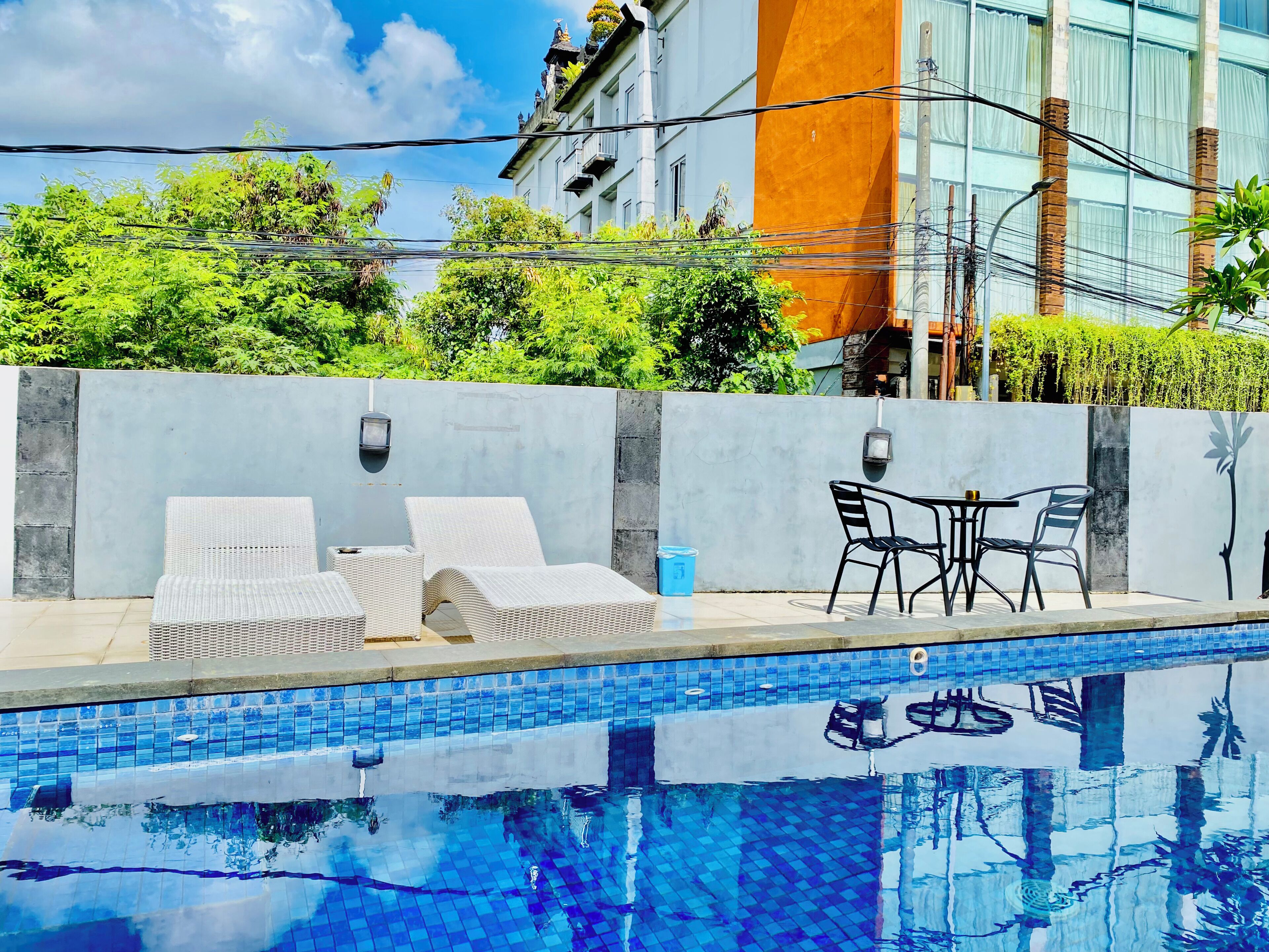 Piscina con sillas de descanso y una mesa, rodeada por un muro bajo y follaje.