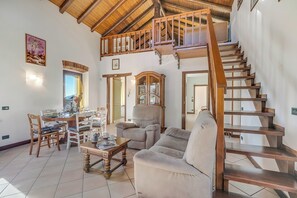 A spacious living area with a wooden staircase, a dining table with chairs, a sofa, and a wooden cabinet. - Il Borgo Del Vergante Casa Maria AC Terrace and Garden, Nebbiuno, Italy (Nebbiuno)