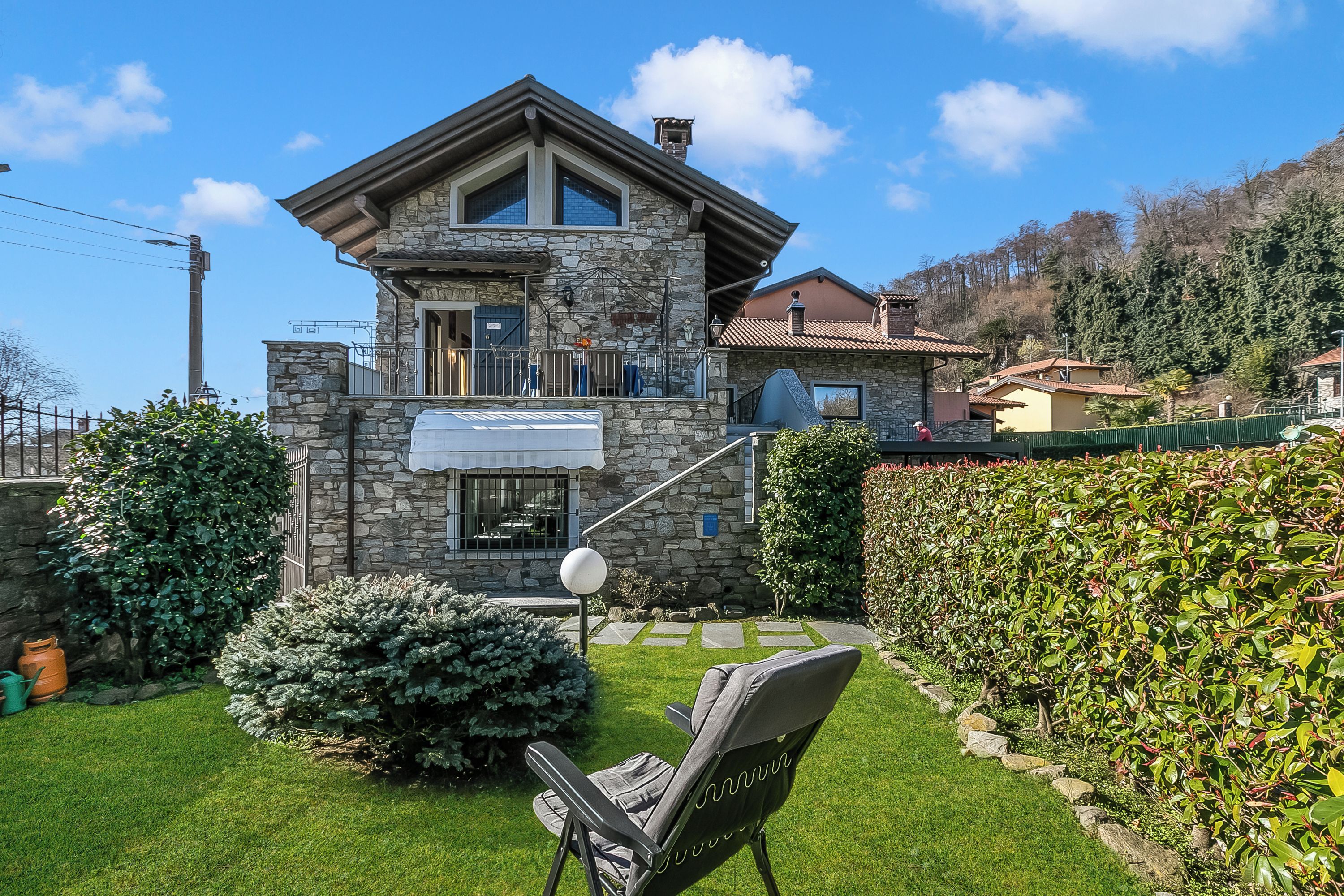 Une maison en pierre avec un balcon, une pelouse et une chaise.