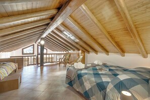A spacious attic bedroom with a sloped ceiling, a large bed, a chair, and a view of the outside. - Il Borgo Del Vergante Casa Maria AC Terrace and Garden, Nebbiuno, Italy (Nebbiuno)
