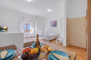 Ein Zimmer mit einem Bett, einem Tisch mit Früchten und einer Flasche sowie einem Gemälde an der Wand.