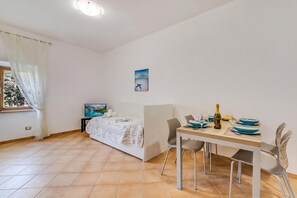 Un dormitorio con cama, mesita de noche, televisor y ventana con cortinas.