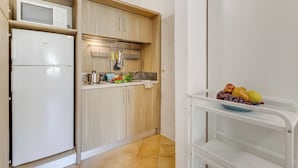 A compact kitchen with a microwave, refrigerator, wooden cabinets, and a fruit bowl on a white shelf. - Residence Argentiera Studio 12 Standard, Miniera dell’Argentiera, Italy (Miniera dell’Argentiera)