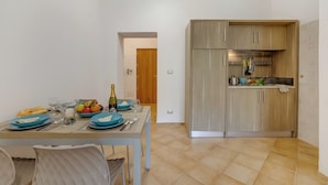 A dining area with a table set for two, a kitchen with wooden cabinets, and a tiled floor. - Residence Argentiera Studio 12 Standard, Miniera dell’Argentiera, Italy (Miniera dell’Argentiera)
