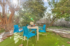 An outdoor dining area with a table and chairs, surrounded by trees and greenery.